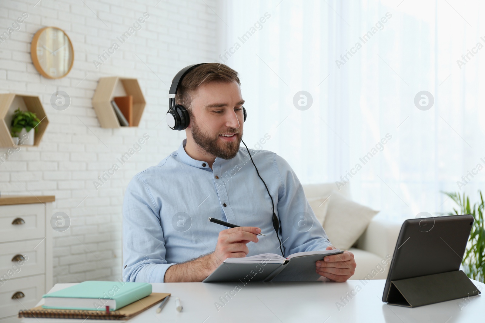 Photo of Young man taking notes during online webinar at table indoors