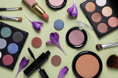 Photo of Flat lay composition with eyeshadow palettes and beautiful flowers on pale olive background
