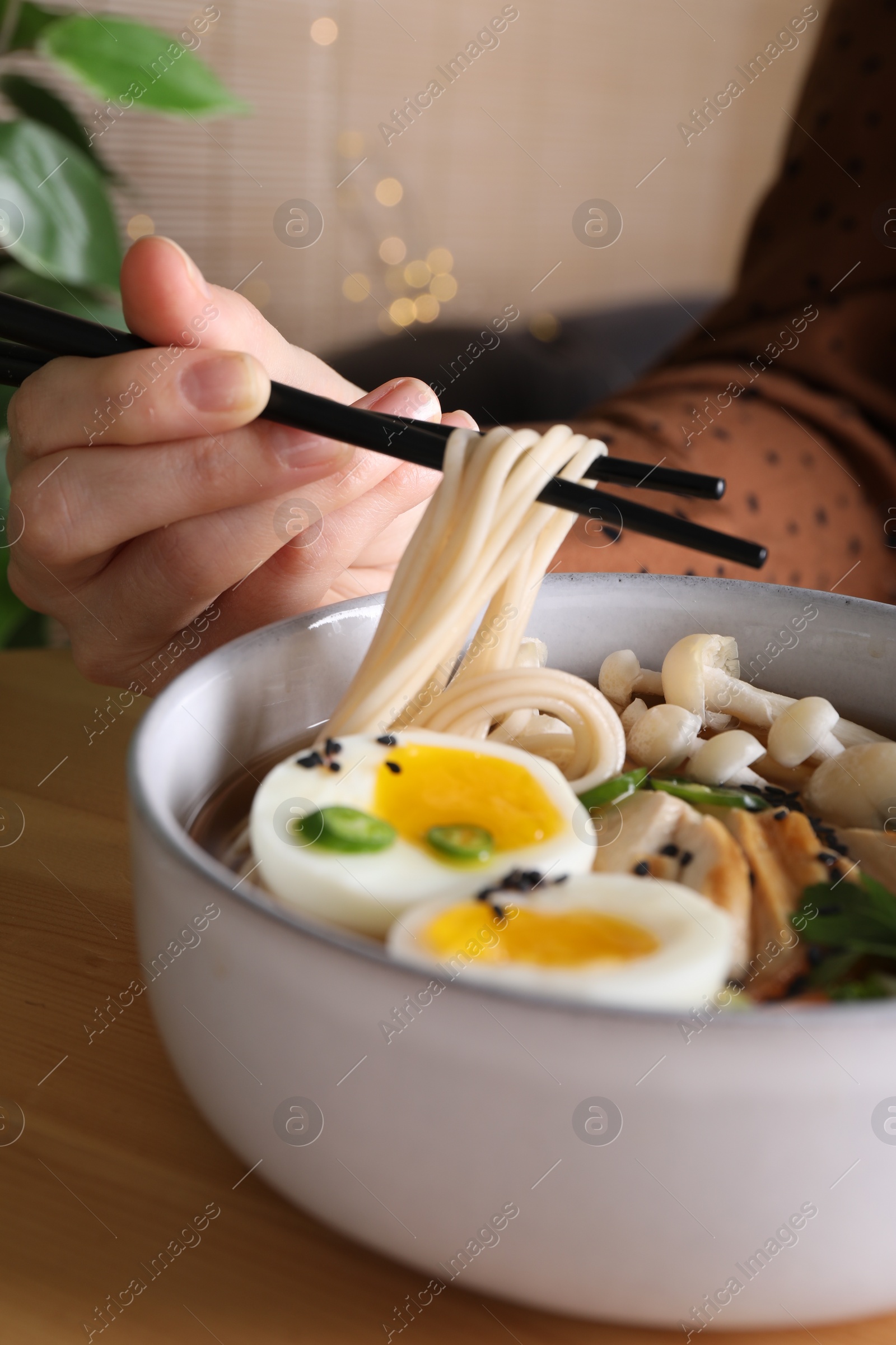 Photo of Woman eating delicious ramen with chopsticks at wooden table, closeup. Noodle soup