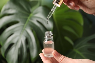 Photo of Woman dripping cosmetic serum from pipette into bottle on blurred background, closeup