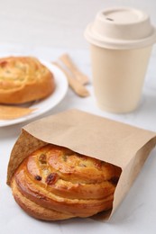 Photo of Delicious roll with raisins in paper bag on white table, closeup. Sweet bun