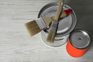 Photo of Can of orange paint, bucket and brushes on white wooden table. Space for text