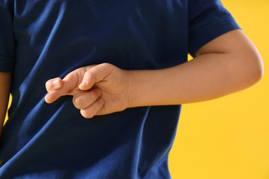 Little boy with crossed fingers on yellow background, closeup. April fool's day