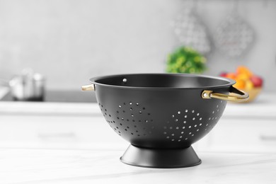 Photo of Black colander on white marble table in kitchen. Space for text