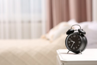 Photo of Black alarm clock on white nightstand indoors. Space for text