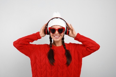 Young woman listening to music with headphones on grey background