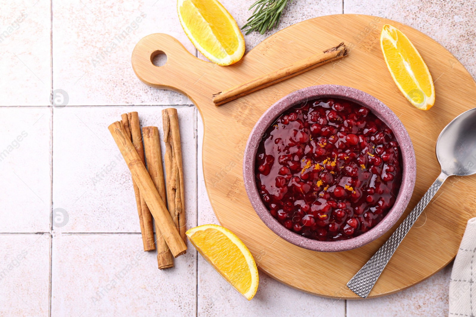 Photo of Tasty cranberry sauce in bowl and ingredients on white tiled table, flat lay. Space for text