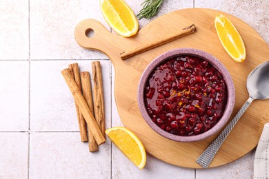 Photo of Tasty cranberry sauce in bowl and ingredients on white tiled table, flat lay. Space for text