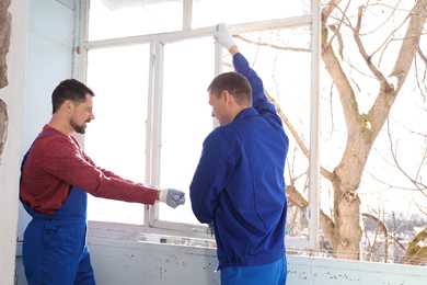 Workers dismantling old window with crowbar indoors