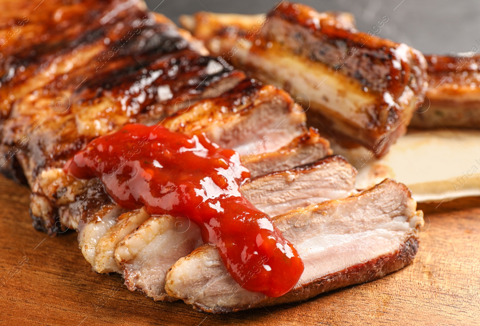 Photo of Delicious grilled ribs with sauce on wooden table, closeup