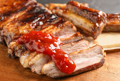 Delicious grilled ribs with sauce on wooden table, closeup