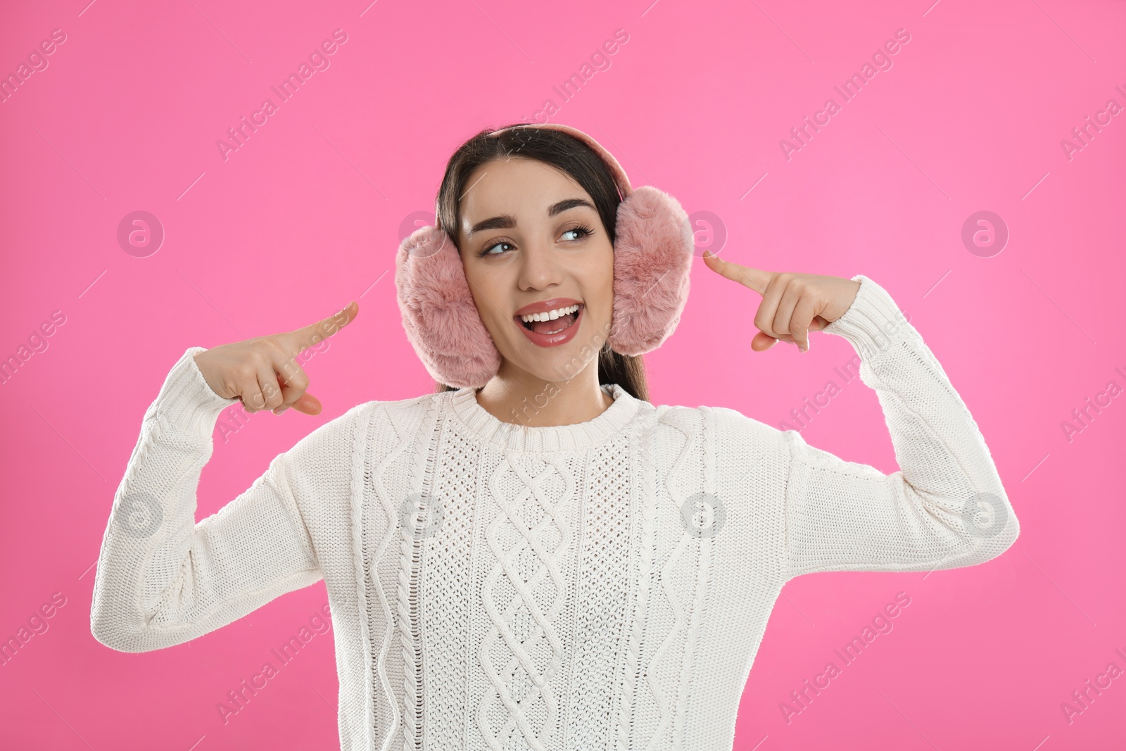 Photo of Beautiful young woman wearing earmuffs on pink background