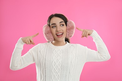 Beautiful young woman wearing earmuffs on pink background