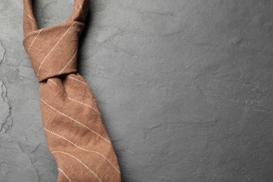 One striped necktie on grey textured table, top view. Space for text