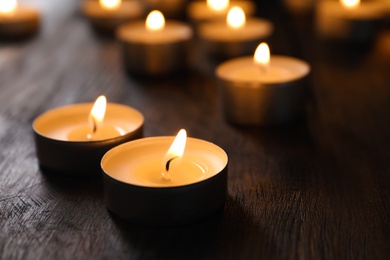 Photo of Wax candles burning on table in darkness, closeup