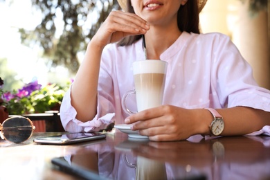 Beautiful young woman with coffee at table in outdoor cafe, closeup