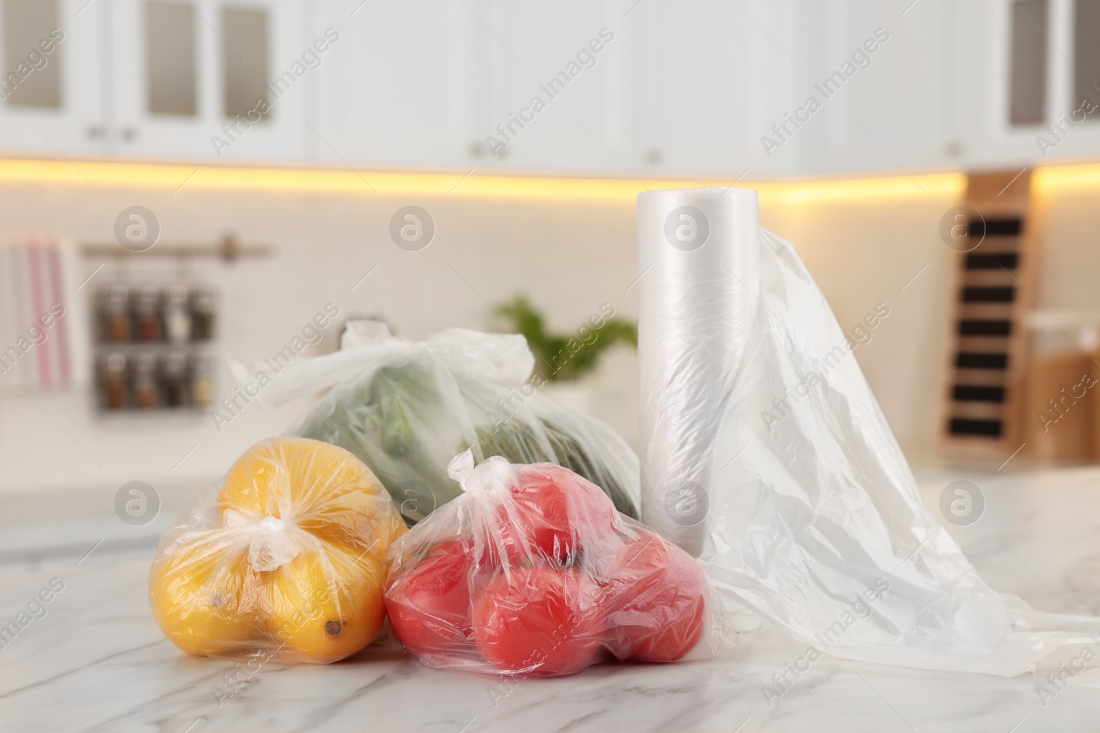 Photo of Plastic bags with different fresh products on white marble table in kitchen