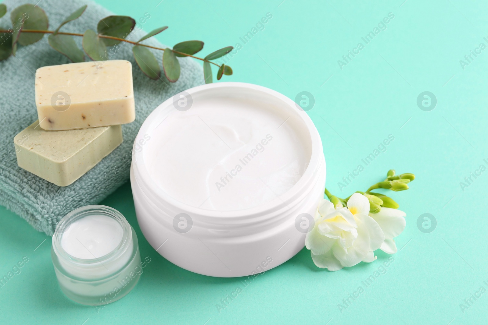 Photo of Moisturizing cream in open jars, soap bars and freesia flower on turquoise background. Body care products