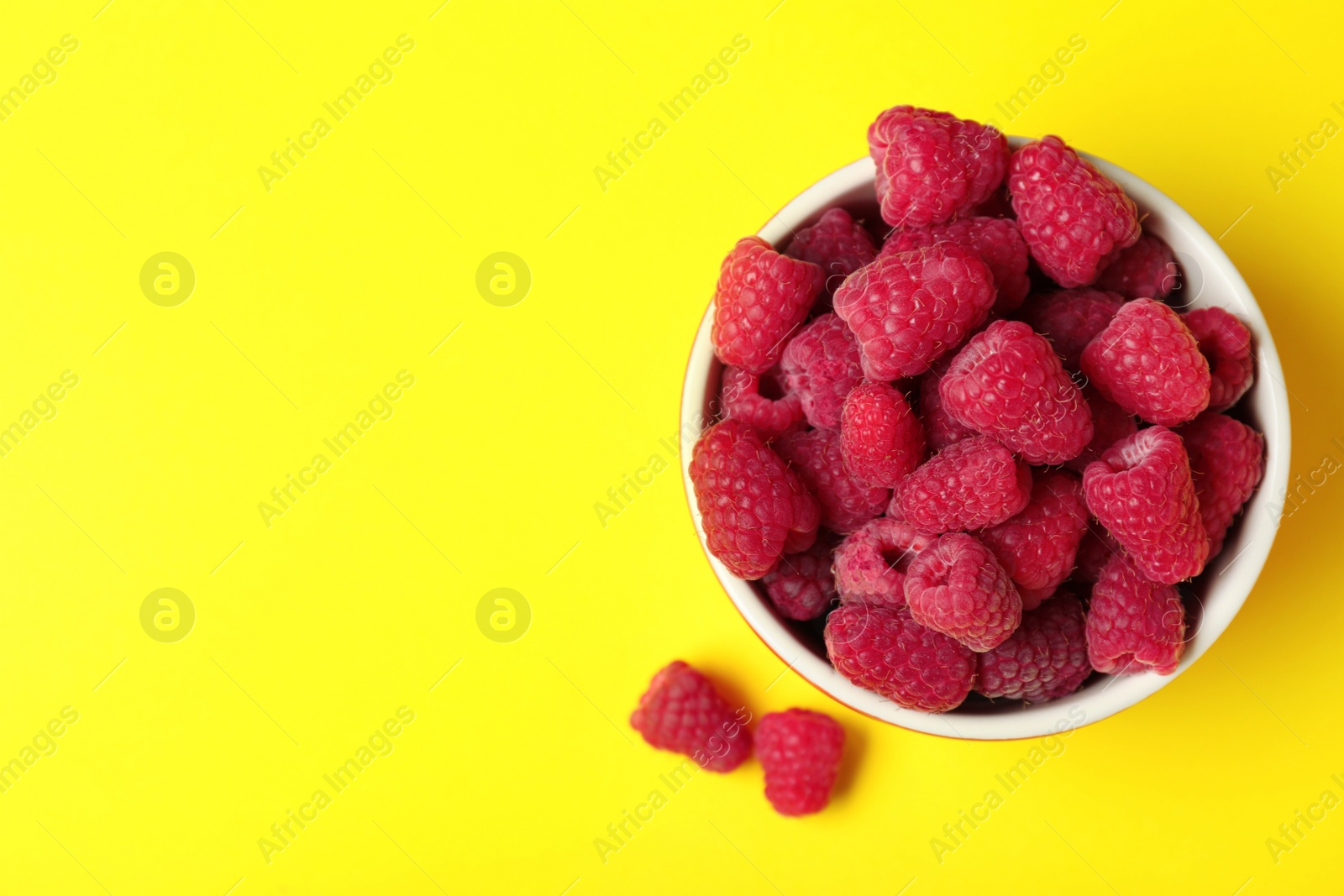 Photo of Bowl of delicious ripe raspberries on yellow background, top view. Space for text