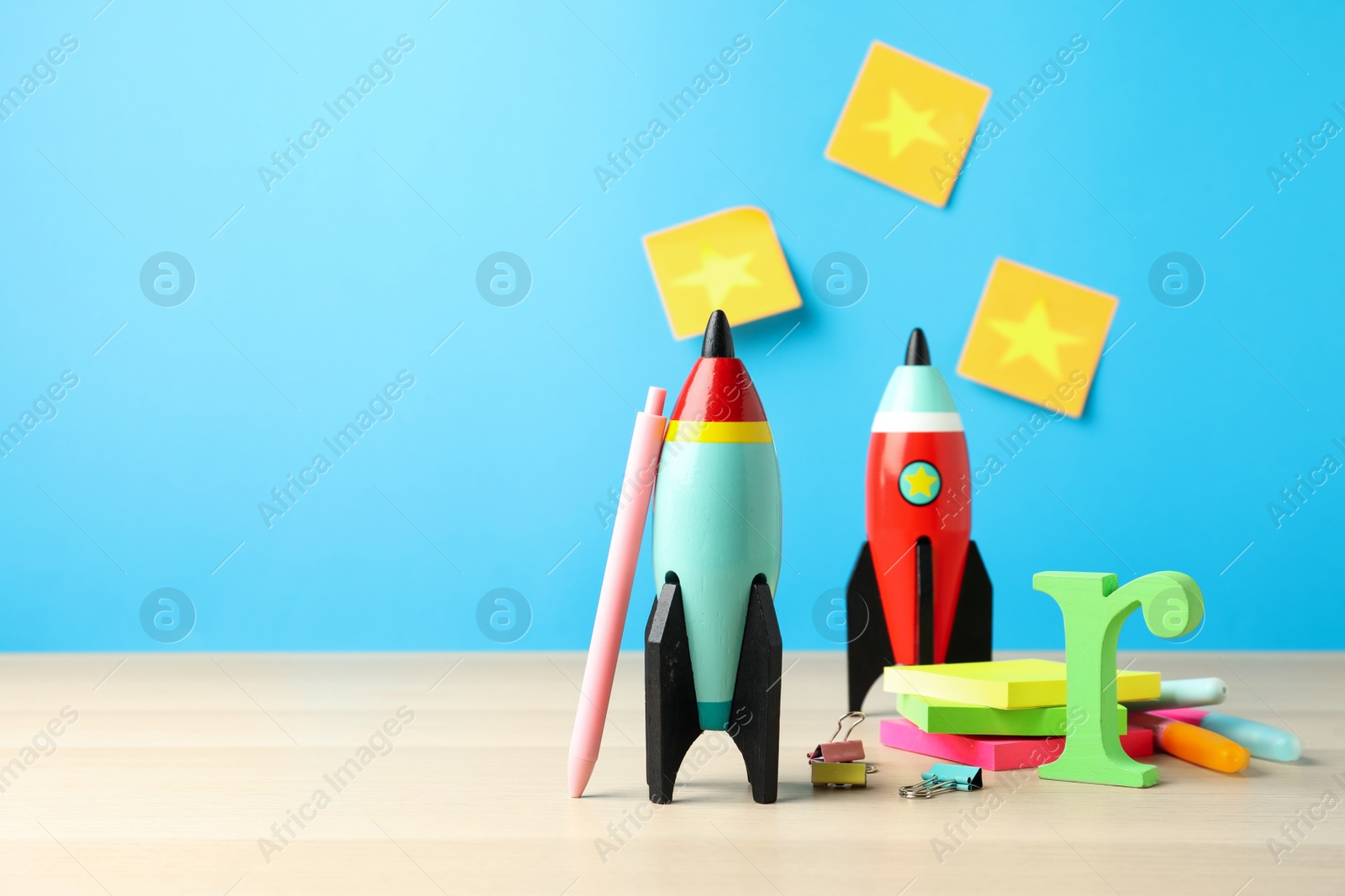 Photo of Bright toy rockets and school supplies on wooden table. Space for text