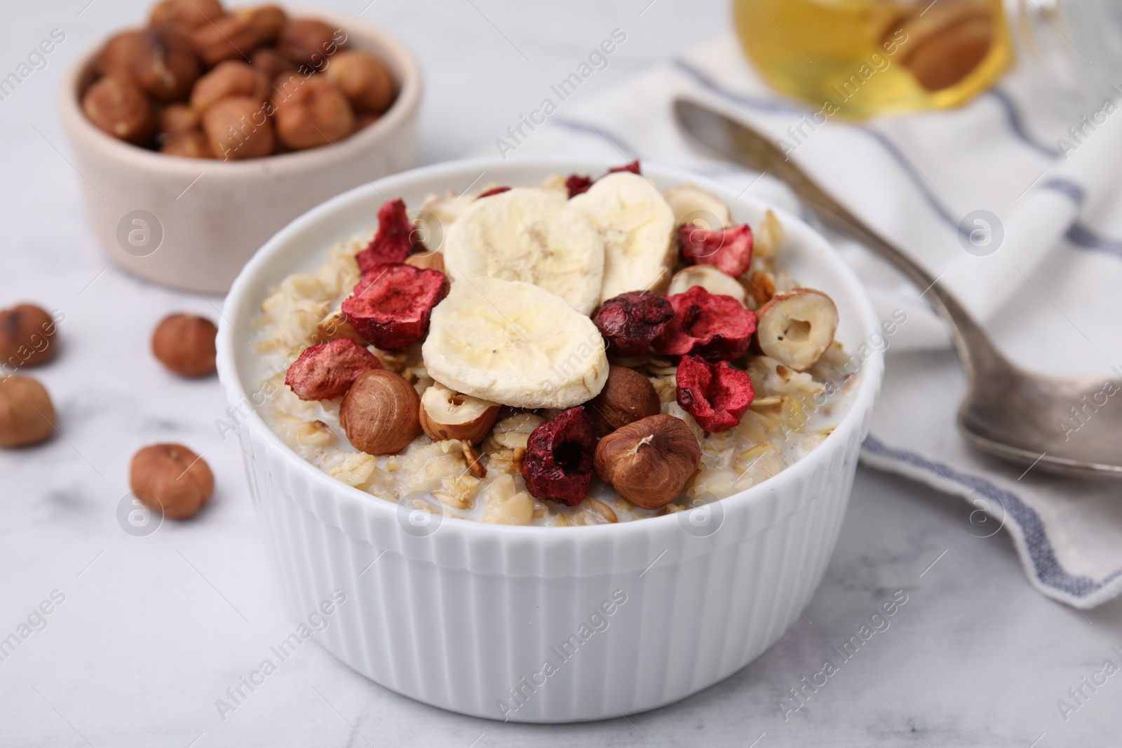 Photo of Delicious oatmeal with freeze dried berries, banana and hazelnuts on white marble table, closeup