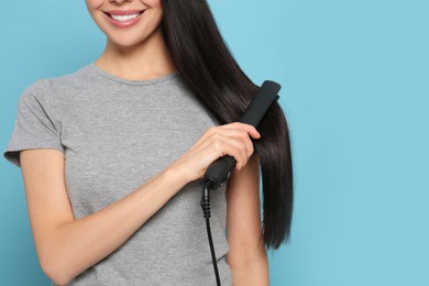 Happy woman using hair iron on light blue background, closeup. Space for text