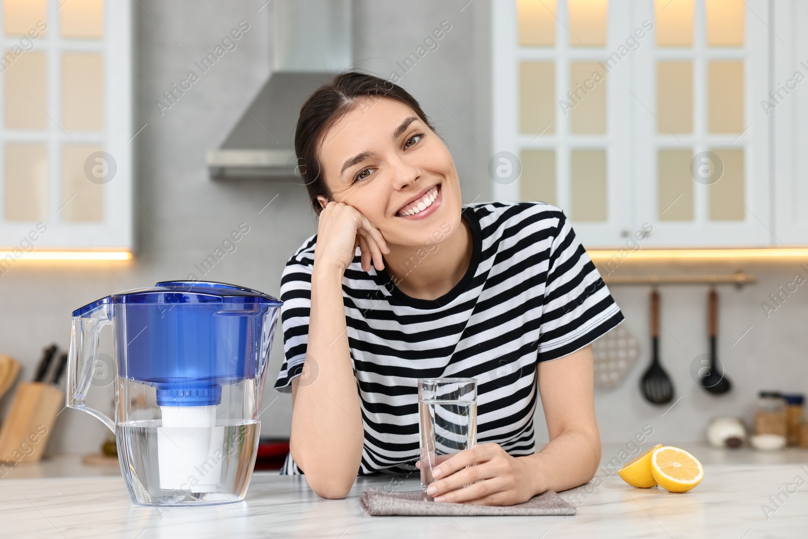 Photo of Woman with glass of water and filter jug in kitchen