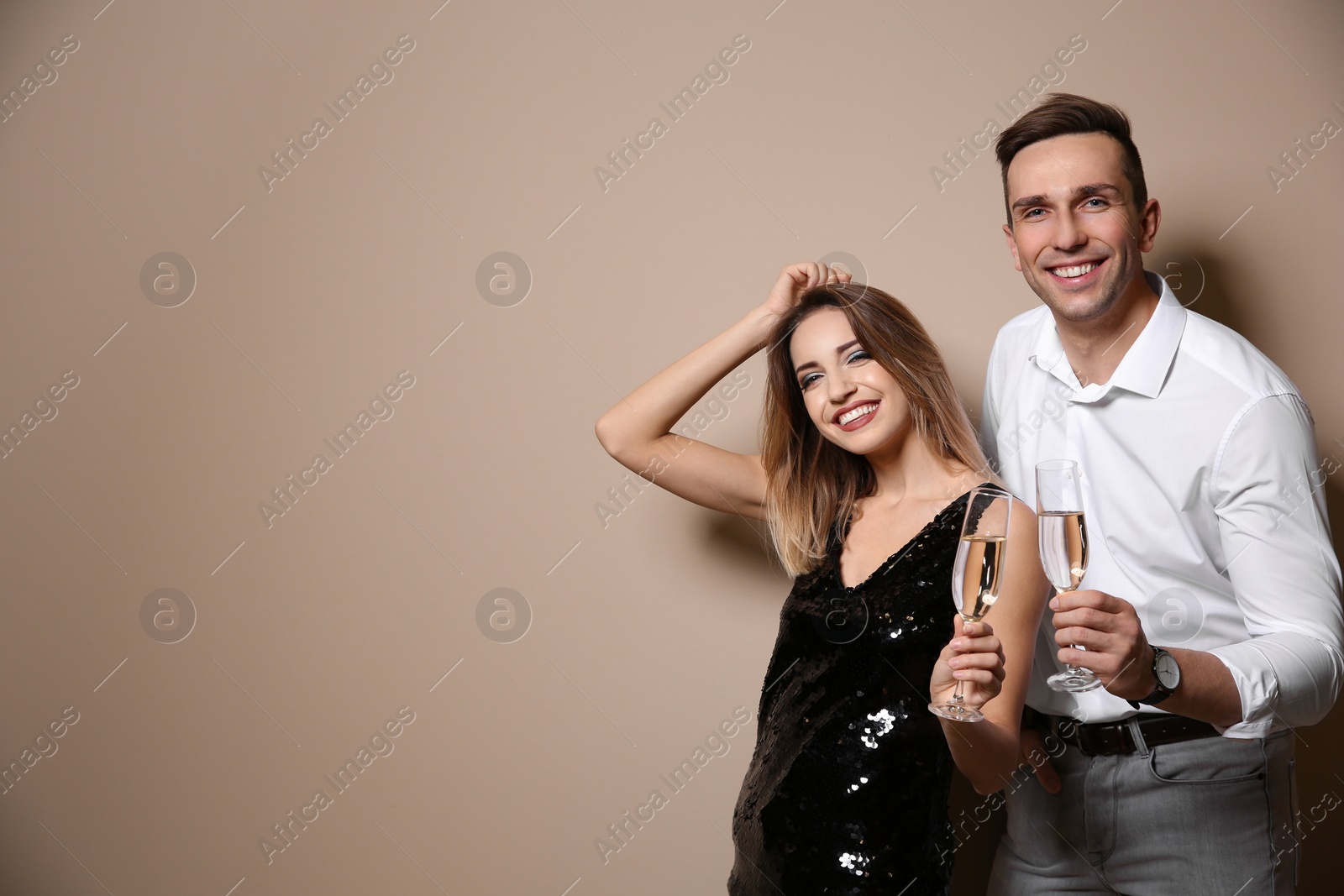 Photo of Happy couple with glasses of champagne on color background. Space for text