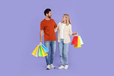 Family shopping. Happy couple with many colorful bags on violet background