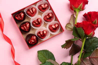 Photo of Box of heart shaped chocolate candies and bouquet on pink background, flat lay