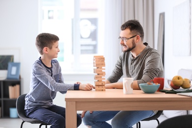 Photo of Little boy and his dad playing board game together at home