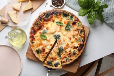 Taking piece of delicious homemade quiche and ingredients on white table, flat lay