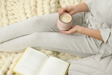 Photo of Woman with cup of coffee and book sitting on soft plaid, closeup