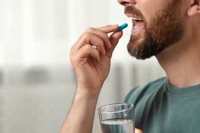 Man with glass of water taking pill indoors, closeup. Space for text