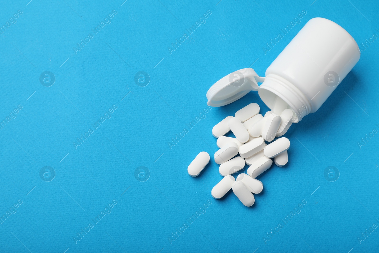 Photo of Vitamin pills and bottle on light blue background, top view. Space for text