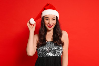 Photo of Christmas celebration. Beautiful young woman in stylish dress and Santa hat on red background, space for text