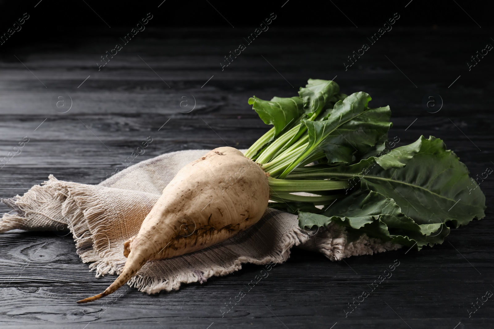 Photo of Fresh sugar beet with leaves on black wooden table