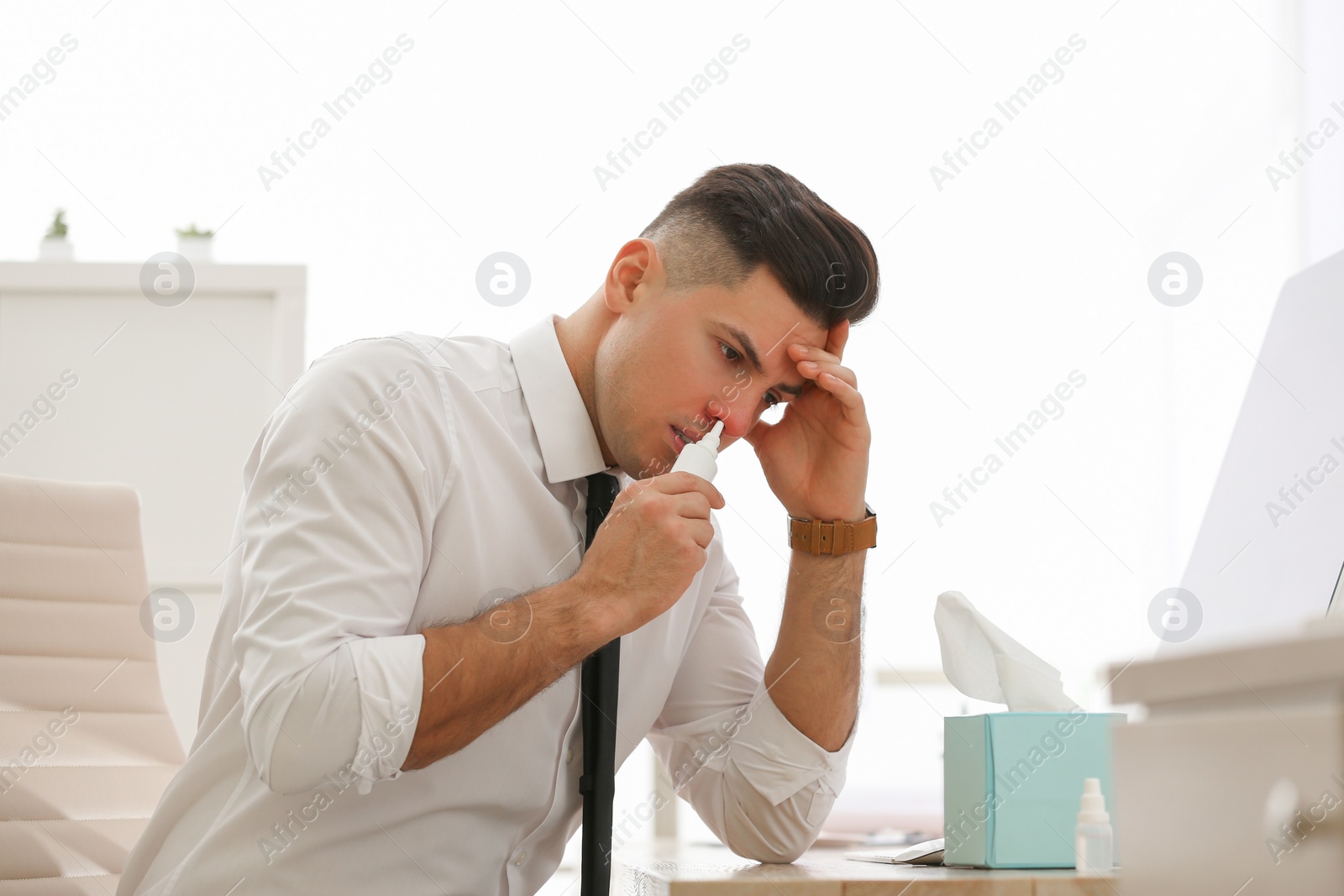 Photo of Ill businessman using nasal spray at table in office