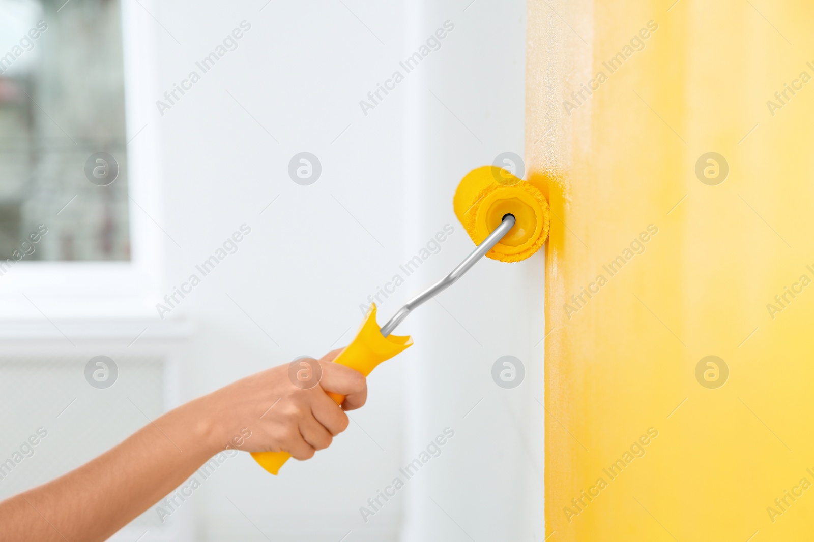 Photo of Woman painting white wall with yellow dye, closeup. Interior renovation