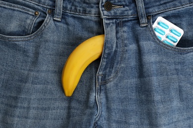 Photo of Banana symbolizing male sexual organ and pills in jeans pocket, top view. Potency problem concept