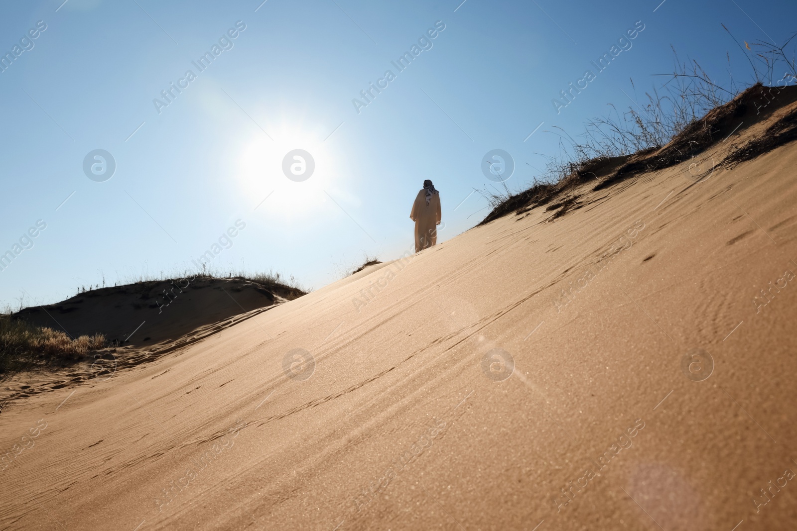 Photo of Man in arabic clothes walking through desert on sunny day, back view