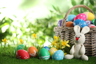 Colorful Easter eggs and toy rabbit on green grass. Space for text