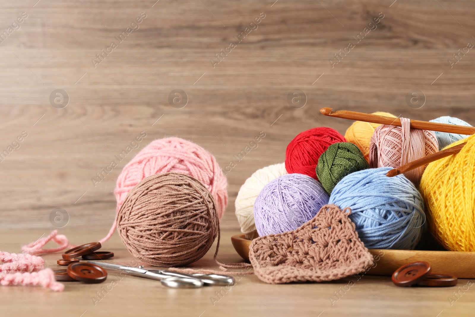 Photo of Clews of colorful knitting threads, crochet hooks, scissors and buttons on wooden table