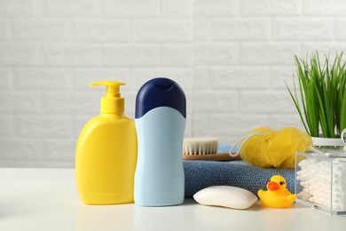 Photo of Baby cosmetic products, bath duck, brush and towel on white table against brick wall