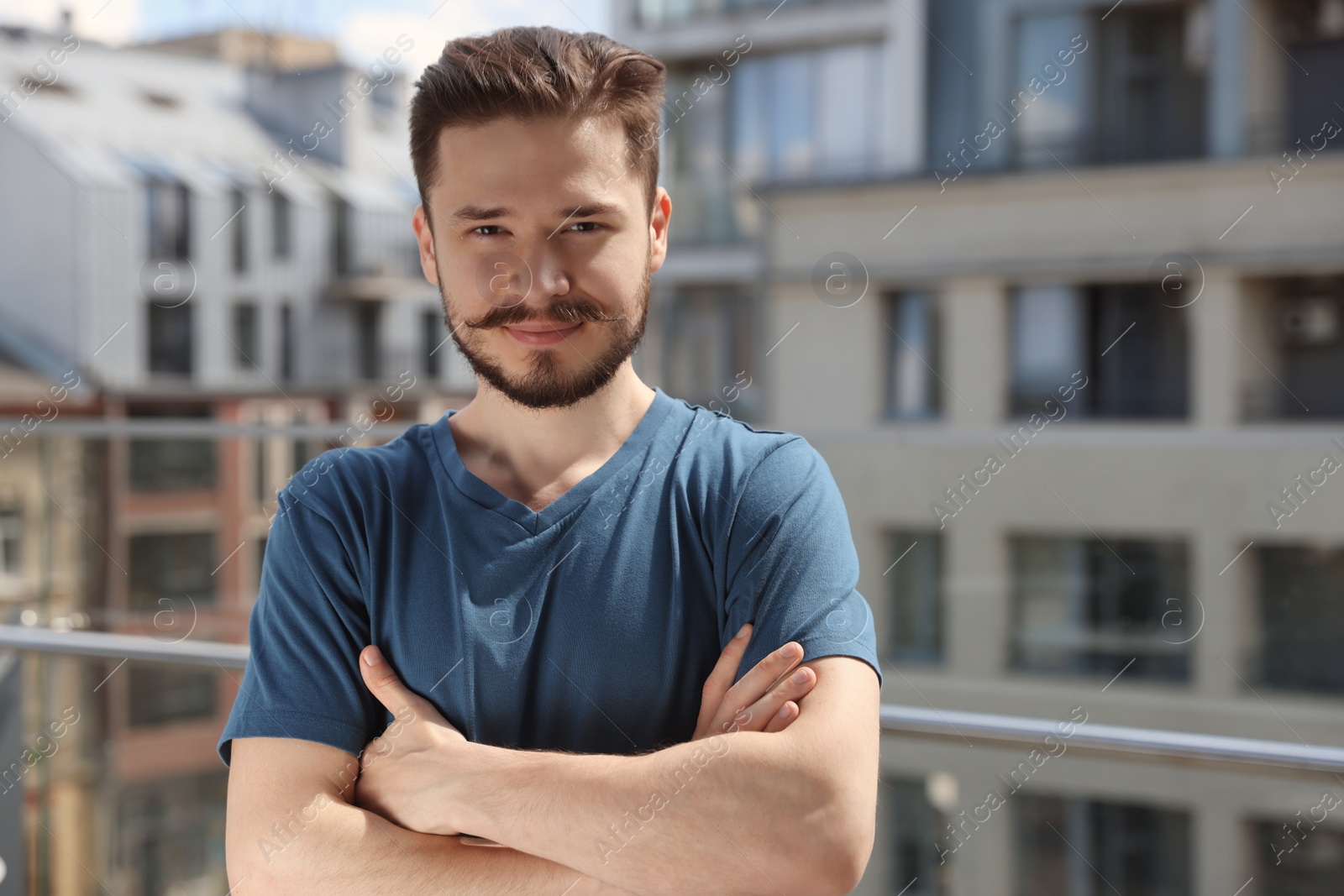 Photo of Handsome man crossing his arms on balcony in city. Space for text