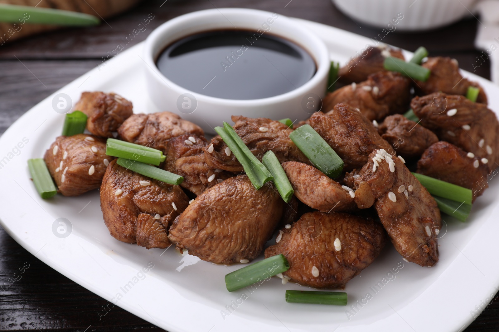 Photo of Plate with tasty soy sauce, roasted meat, sesame and green onion on table, closeup