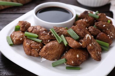 Plate with tasty soy sauce, roasted meat, sesame and green onion on table, closeup