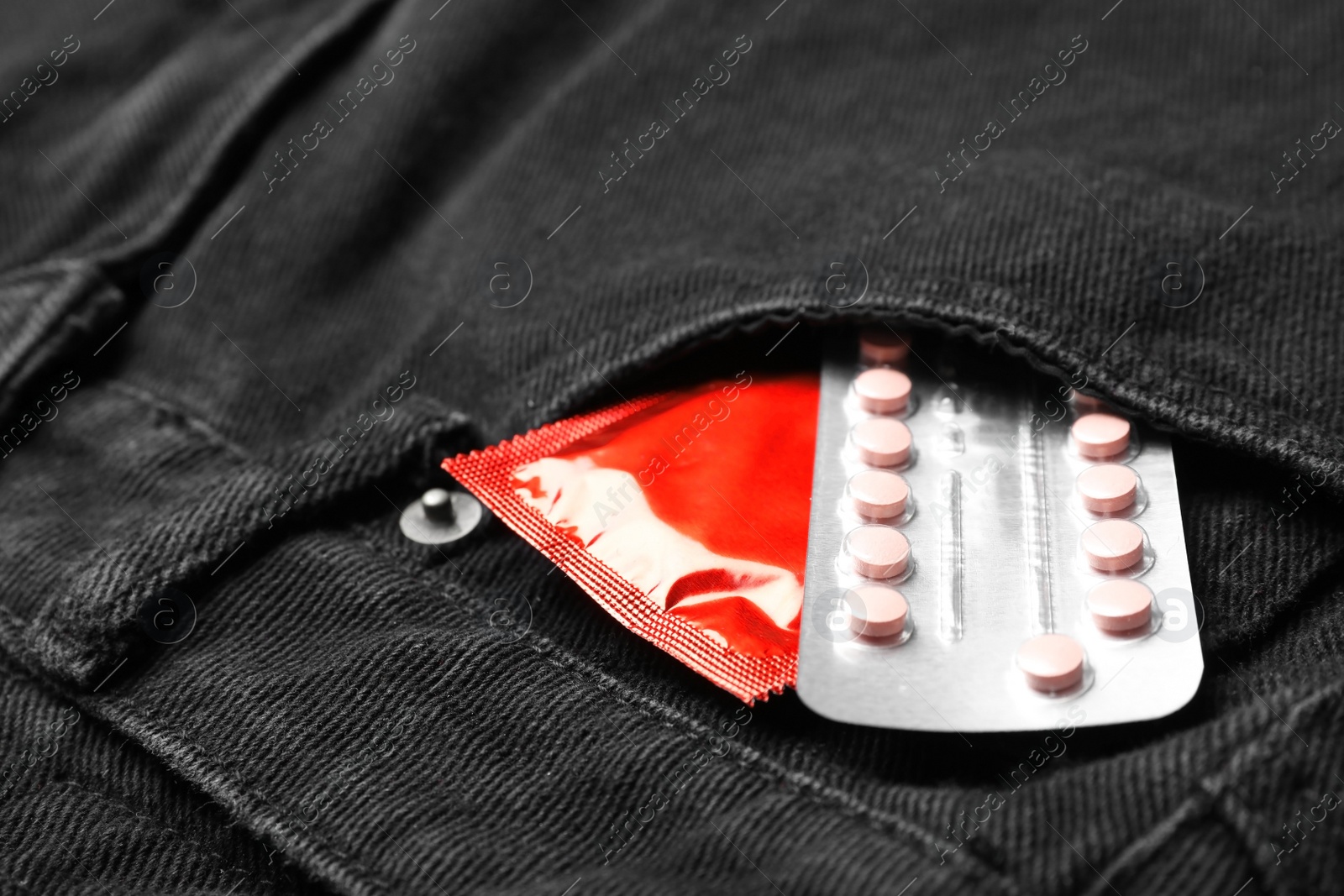 Photo of Red condom and birth control pills in pocket of jeans, closeup. Safe sex concept