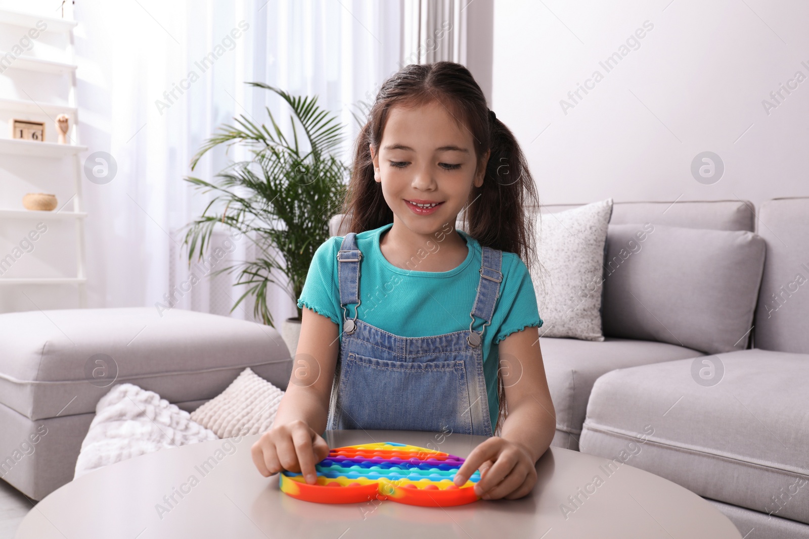 Photo of Little girl playing with pop it fidget toy at table in living room