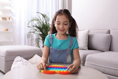 Little girl playing with pop it fidget toy at table in living room